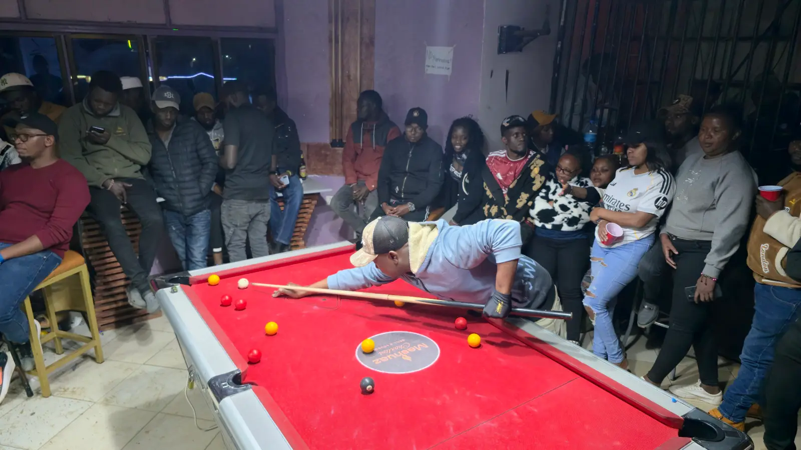 A player lines up a shot as a mixed crowd of young men and women watches at the King's Pool Tournament