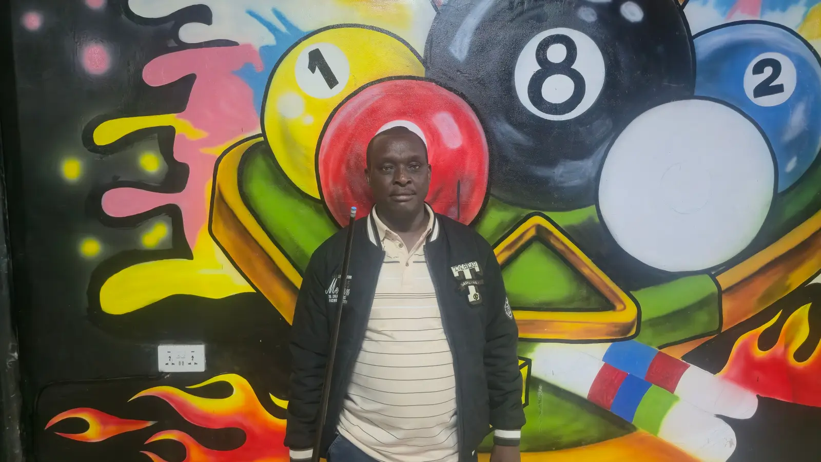 Hon. James Kuya Nina with a cue in front of a pool-themed mural