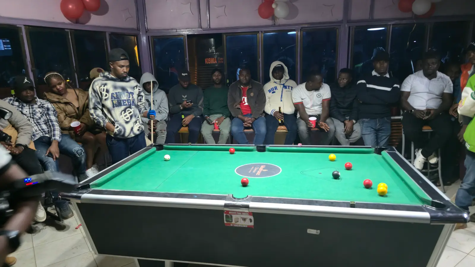 The crowd seated around the green table during a late match
